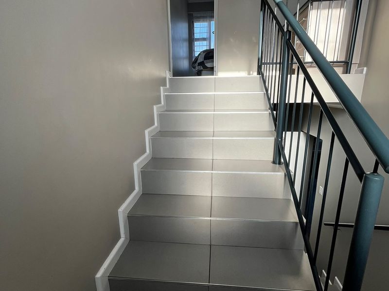 A clean, modern staircase featuring tiled steps and a sturdy metal balustrade, providing access to the upper level of the apartment.