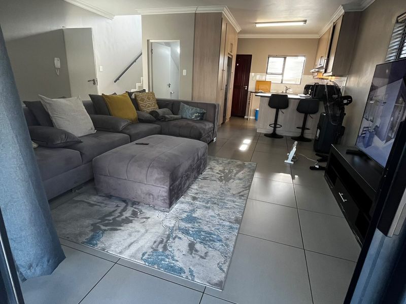 Open-plan living area featuring tiled flooring, a functional kitchen with a breakfast bar, and direct access to a staircase.