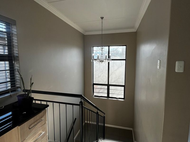 A well-lit hallway featuring a staircase with a metal balustrade, tiled flooring, built-in cabinetry, and a decorative chandelier.