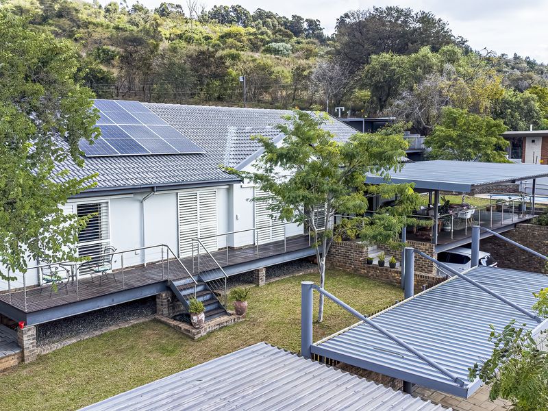 Elevated rear view of the property featuring a raised timber deck, covered patio area, carport, and solar panels installed on the tiled roof.