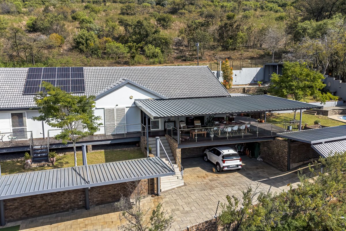 Aerial view of the rear elevation featuring a raised timber deck, covered patio, paved driveway, solar panels, and a swimming pool set in a landscaped garden.