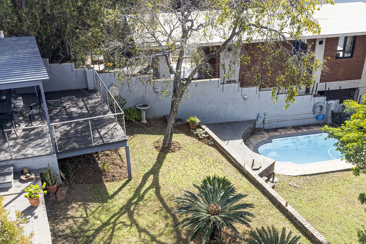 Aerial view of the rear garden featuring a swimming pool, a raised timber deck with a covered patio area, and established landscaping.