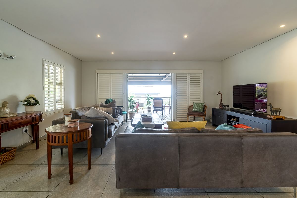 Spacious living room featuring neutral tiled flooring, recessed downlighting, and plantation shutters, with seamless access to an outdoor patio area.