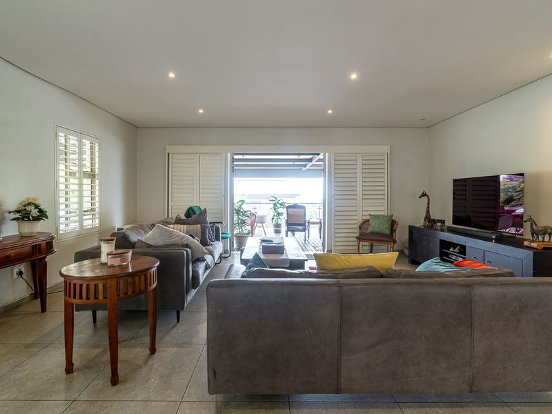 Spacious living room featuring neutral tiled flooring, recessed downlighting, and plantation shutters, with seamless access to an outdoor patio area.