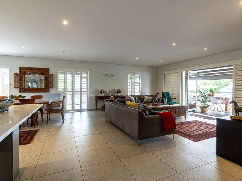 Spacious open-plan living and dining area featuring large-format floor tiles, recessed lighting, and plantation shutters, with seamless flow to an outdoor patio.