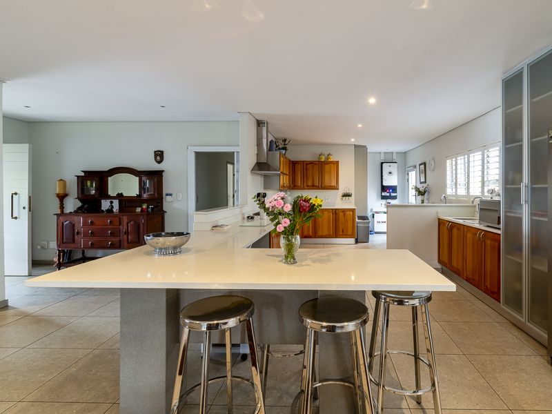 Spacious open-plan kitchen featuring a central island with stone countertops, wooden cabinetry, and tiled flooring, offering a functional and well-maintained cooking and dining space.
