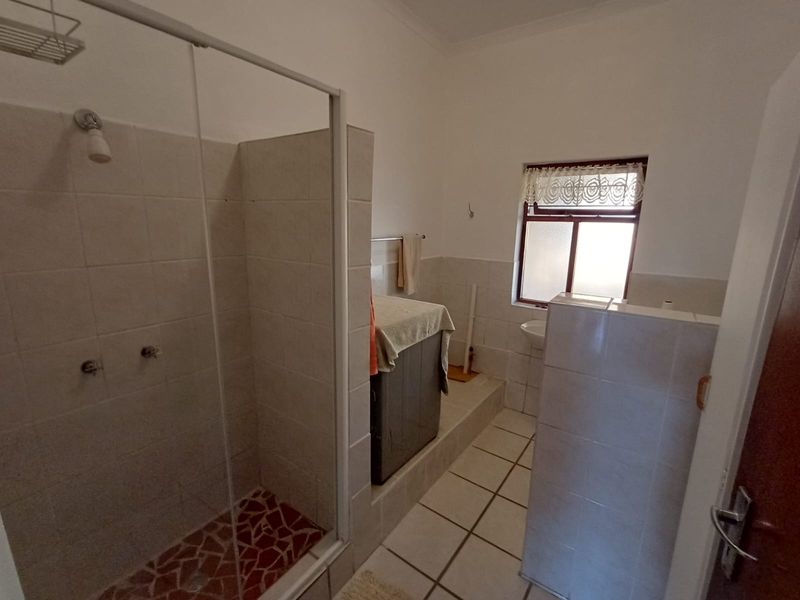 A functional bathroom featuring a walk-in shower with a glass enclosure, tiled walls, and tiled flooring on a raised platform area.