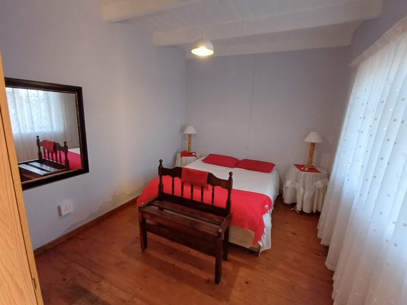A bedroom featuring exposed ceiling beams and timber flooring, showing signs of wall surface deterioration and damp staining.