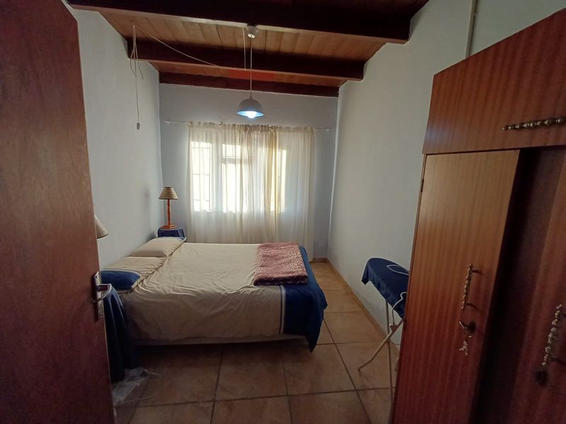A bedroom featuring exposed timber ceiling beams, tiled flooring, and a built-in wardrobe, offering a functional space with potential for cosmetic updates.