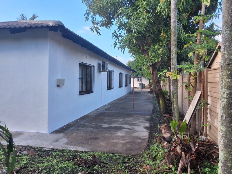 A view of the rear exterior of the house featuring a concrete pathway, security bars on windows, and a precast boundary wall.