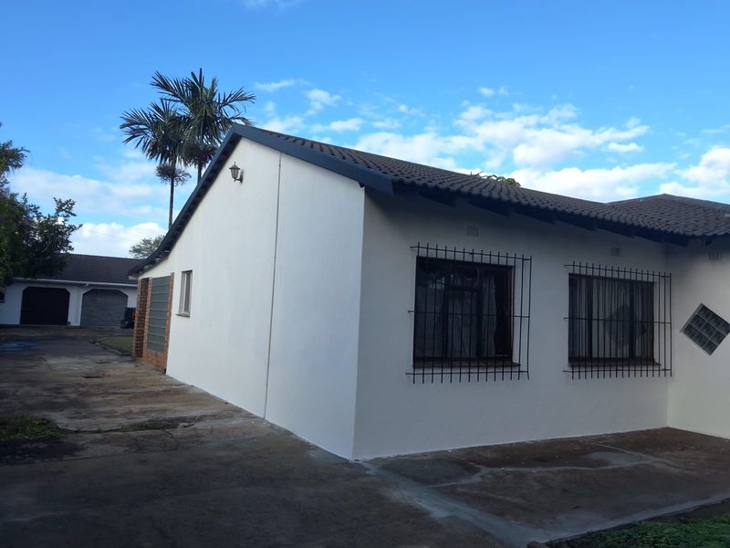 Rear view of the house featuring a tiled roof, security bars on windows, and a concrete driveway area.