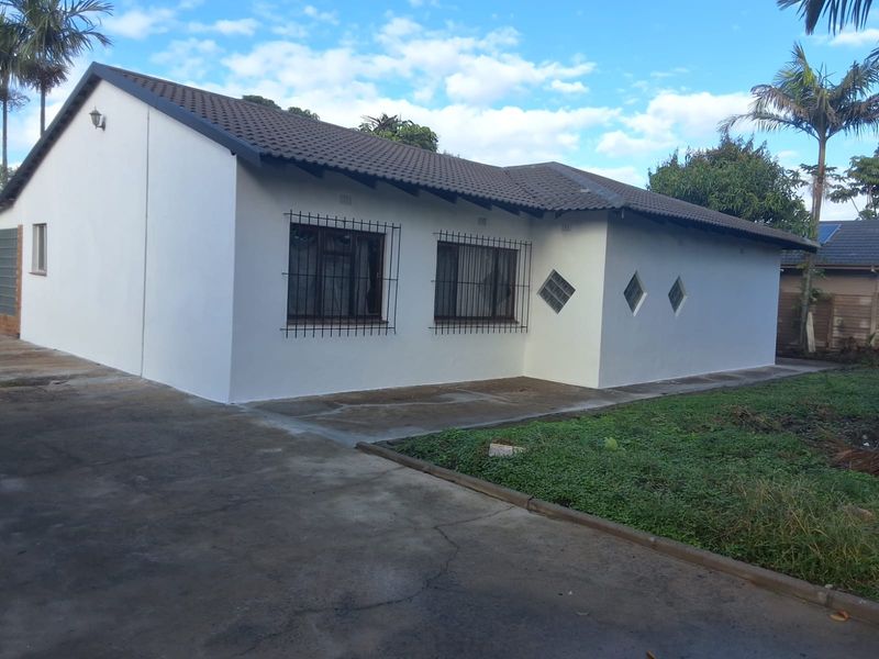 Rear view of a single-story house featuring a tiled roof, security bars on windows, and decorative glass block accents with an adjacent concrete driveway.