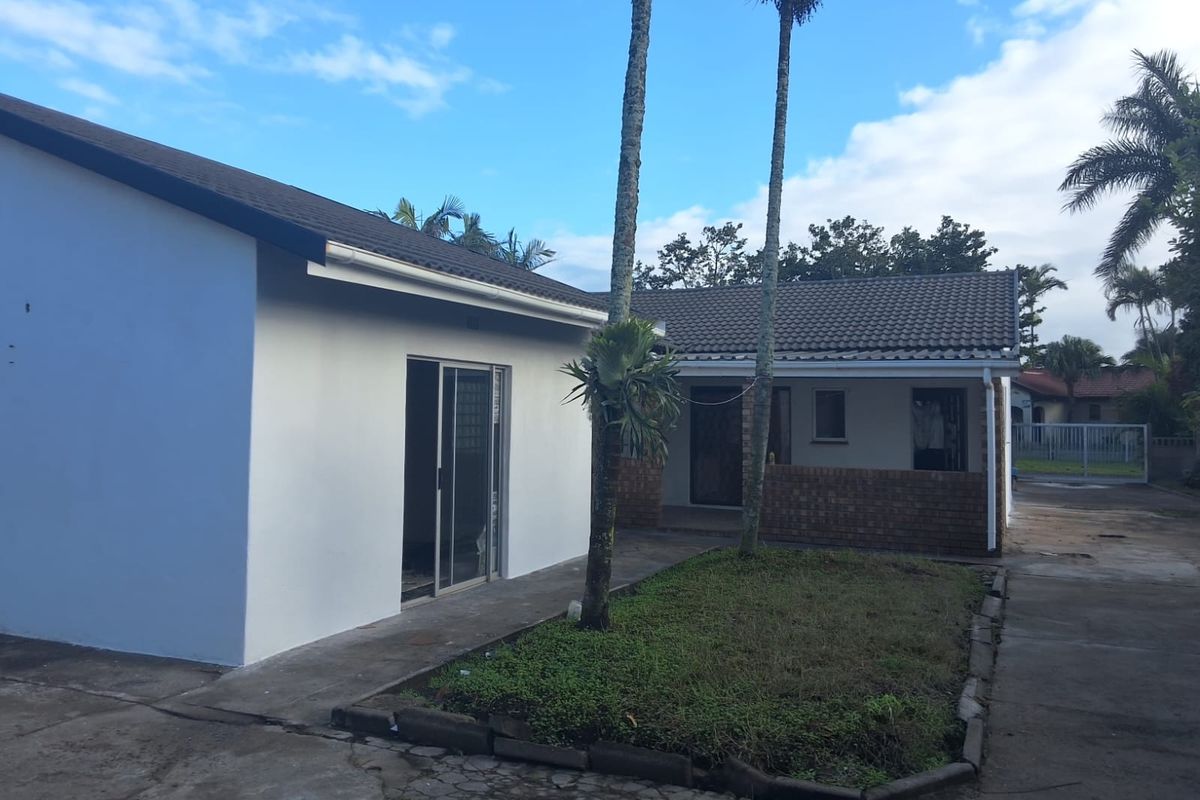 Rear view of the property featuring a concrete driveway, sliding glass door access, and a small garden area with established palm trees.