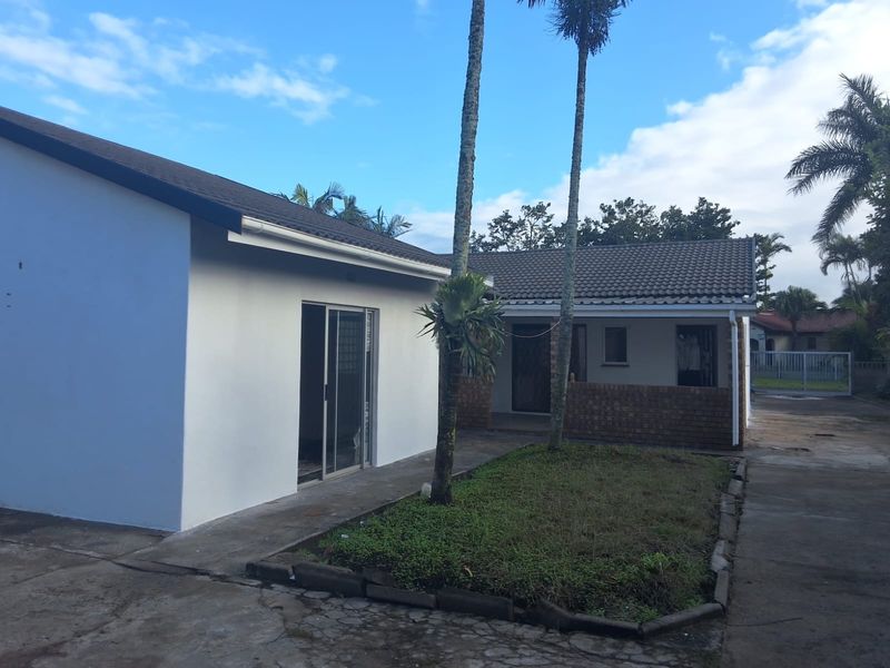 Rear view of the property featuring a concrete driveway, sliding glass door access, and a small garden area with established palm trees.