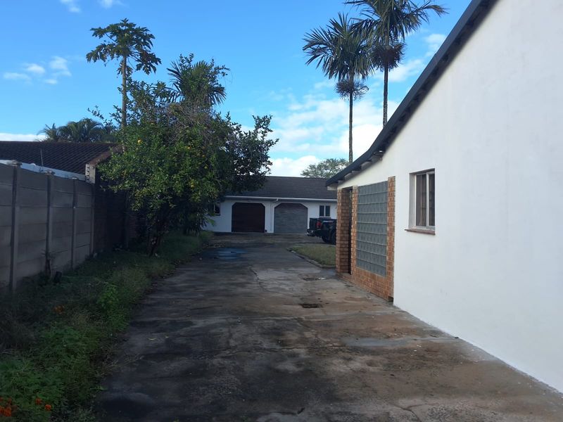 Rear exterior view showing a concrete driveway leading to a double garage, bordered by a precast wall and established garden area.