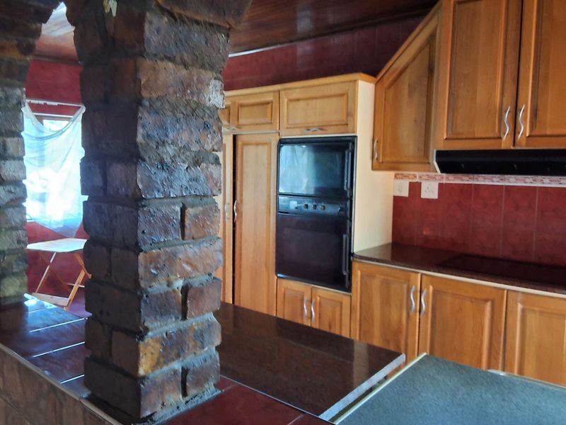 Kitchen featuring wooden cabinetry, built-in oven, extractor fan, and a distinctive exposed brick pillar, with a timber ceiling and tiled backsplash.