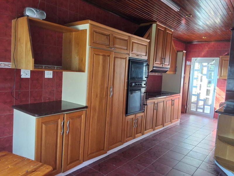 A spacious kitchen featuring extensive wooden cabinetry, built-in appliances, tiled surfaces, and a timber-paneled ceiling with direct access to the exterior.