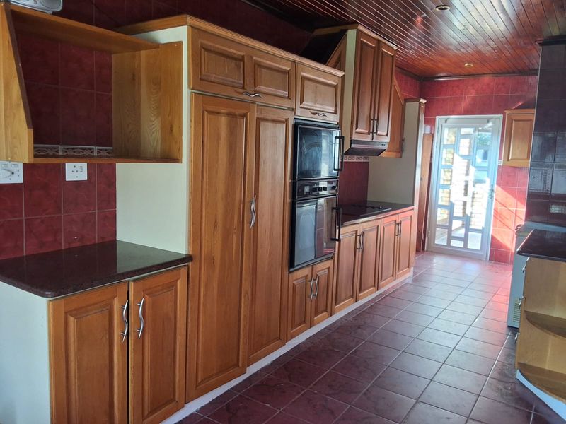 A dated kitchen featuring wooden cabinetry, integrated double oven, tiled flooring, and a timber ceiling with access to an exterior door.