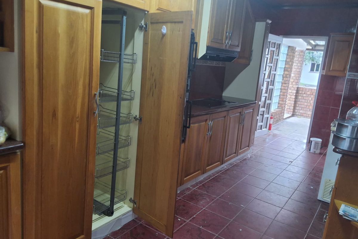 A kitchen featuring wooden cabinetry with a pull-out pantry, integrated hob, extractor fan, and tiled flooring, leading to an outdoor area.