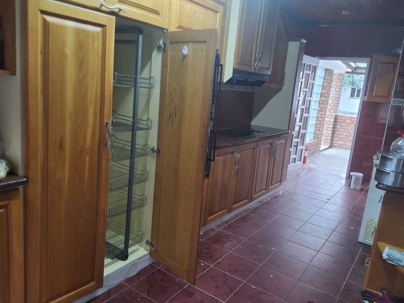 A kitchen featuring wooden cabinetry with a pull-out pantry, integrated hob, extractor fan, and tiled flooring, leading to an outdoor area.