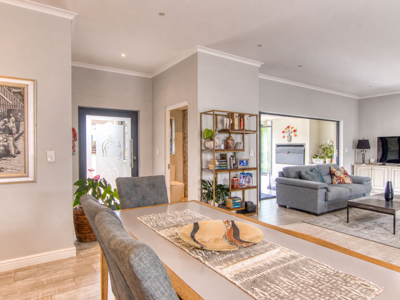 An open-plan living and dining area featuring neutral tones, tiled flooring, recessed lighting, and seamless flow to an outdoor patio space.