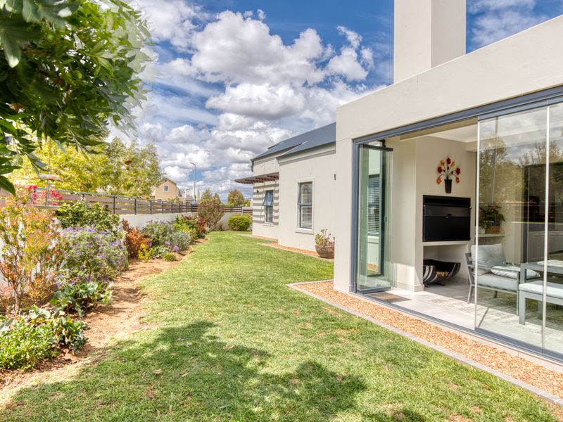 A well-maintained rear garden featuring a landscaped lawn, boundary fencing, and a covered patio area with a built-in fireplace and sliding glass doors.