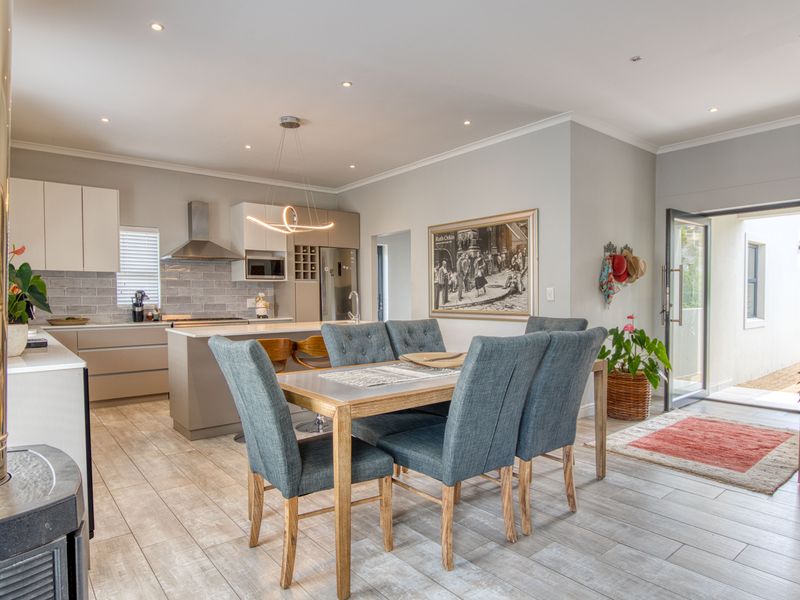 Modern open-plan kitchen and dining area featuring sleek cabinetry, a central island, tiled flooring, and a contemporary wood-burning fireplace.