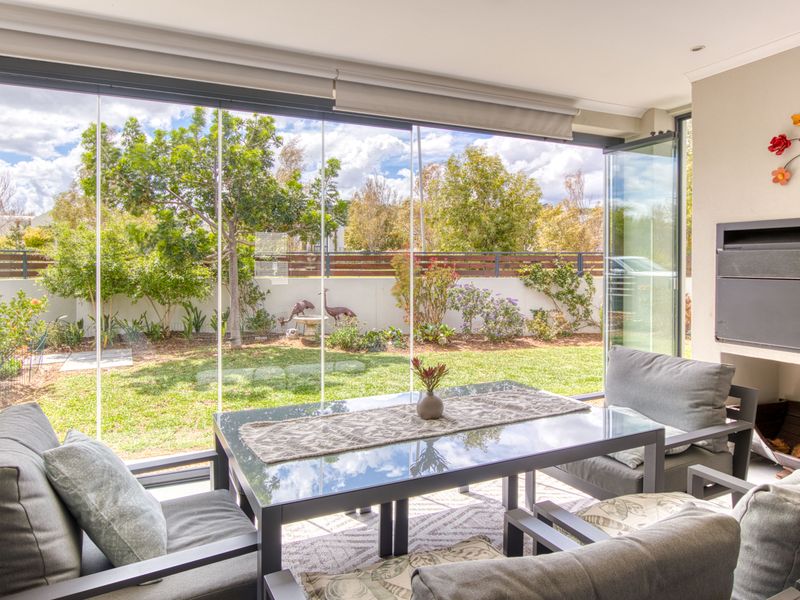 A bright, enclosed patio featuring floor-to-ceiling stacking glass doors, a built-in fireplace, and direct access to the landscaped garden.