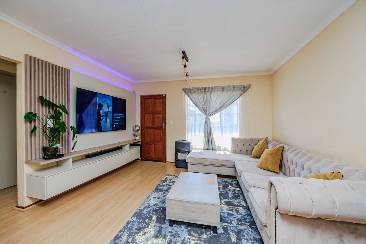 A well-maintained living room featuring laminate flooring, a custom built-in media console with slatted wood paneling, and integrated LED accent lighting.