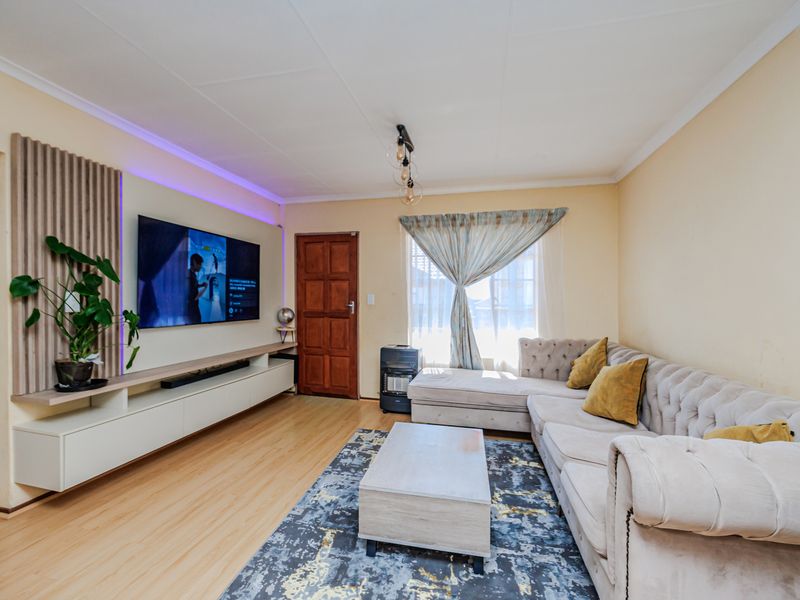 A well-maintained living room featuring laminate flooring, a custom built-in media console with slatted wood paneling, and integrated LED accent lighting.