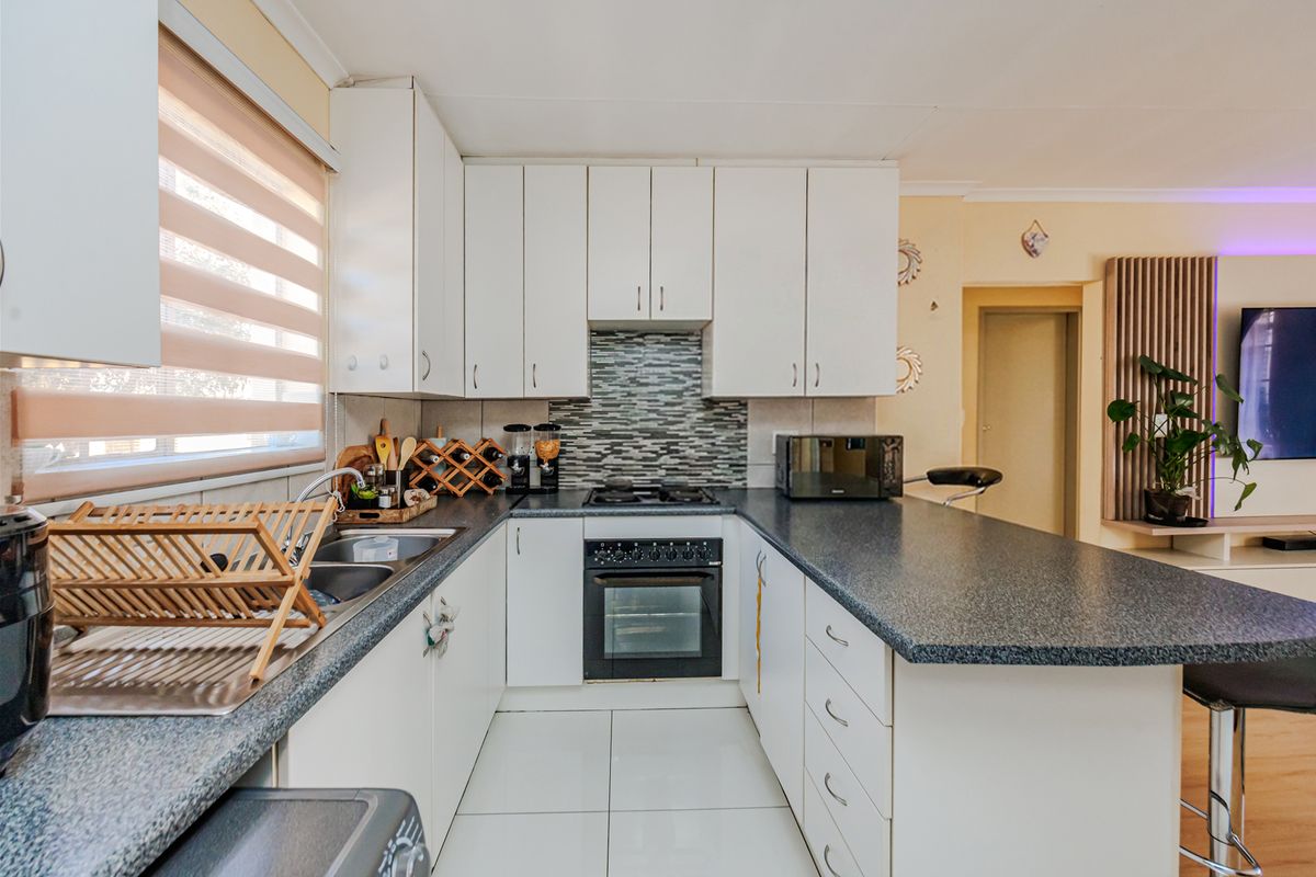 A functional kitchen featuring white cabinetry, dark laminate countertops, a built-in oven with gas hob, and a tiled backsplash.