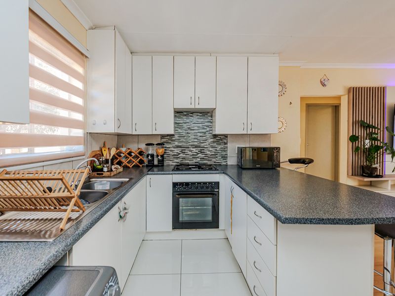 A functional kitchen featuring white cabinetry, dark laminate countertops, a built-in oven with gas hob, and a tiled backsplash.