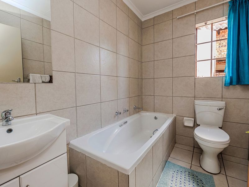 A functional bathroom featuring a built-in vanity, bathtub, and toilet, finished with neutral ceramic wall and floor tiles.