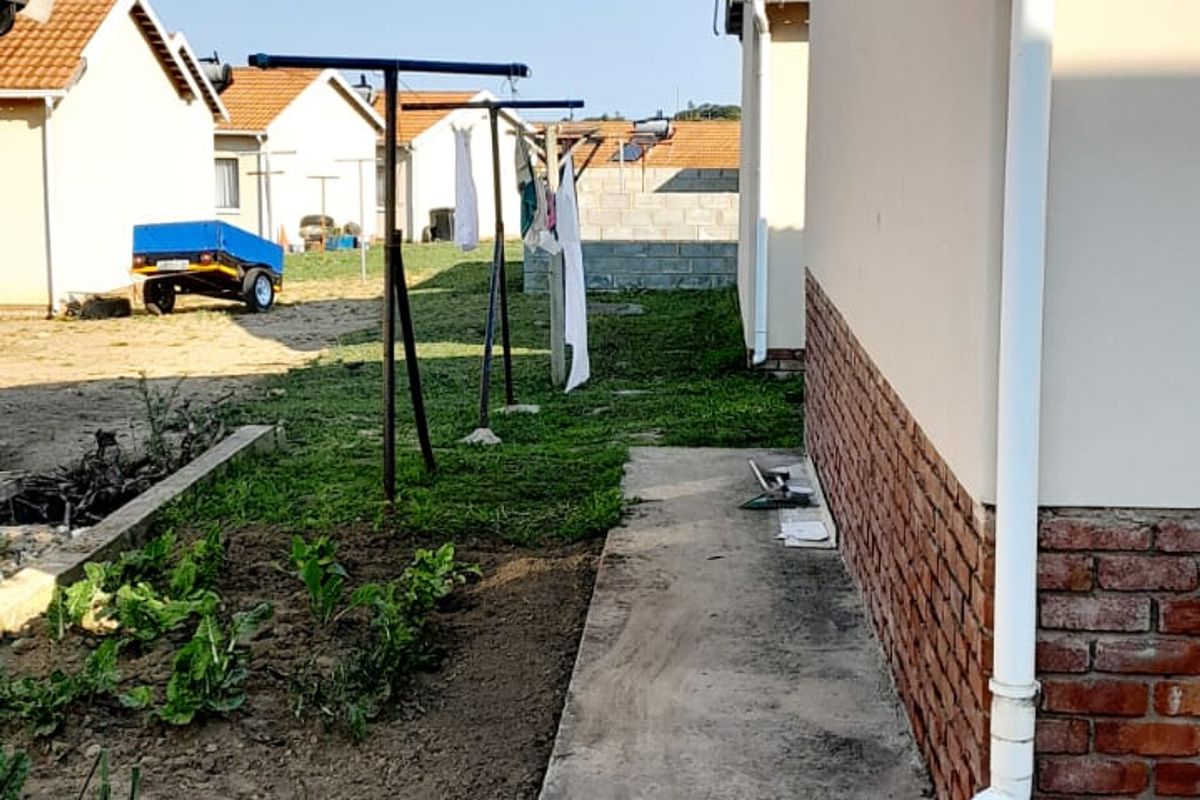 Rear exterior view of the property featuring a concrete pathway, brick plinth detail, and downpipe installation along the side wall.