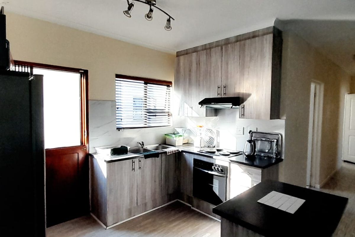 Functional kitchen featuring modern wood-look cabinetry, built-in oven and hob, extractor fan, and a practical layout with direct access to the exterior.