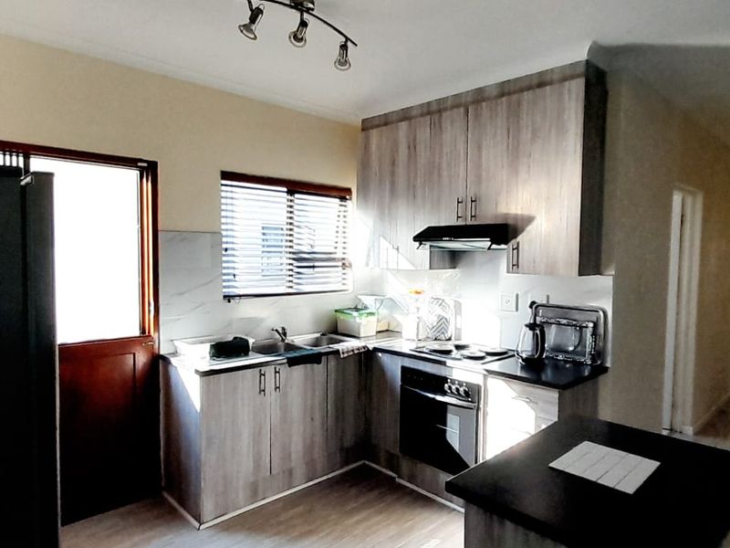 Functional kitchen featuring modern wood-look cabinetry, built-in oven and hob, extractor fan, and a practical layout with direct access to the exterior.