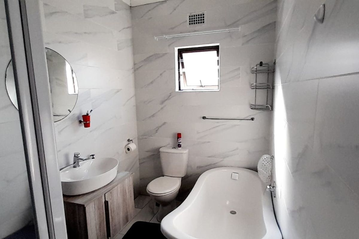 Modern bathroom featuring a freestanding bathtub, vessel sink with vanity cabinet, toilet, and a separate shower enclosure with marble-look wall tiles.