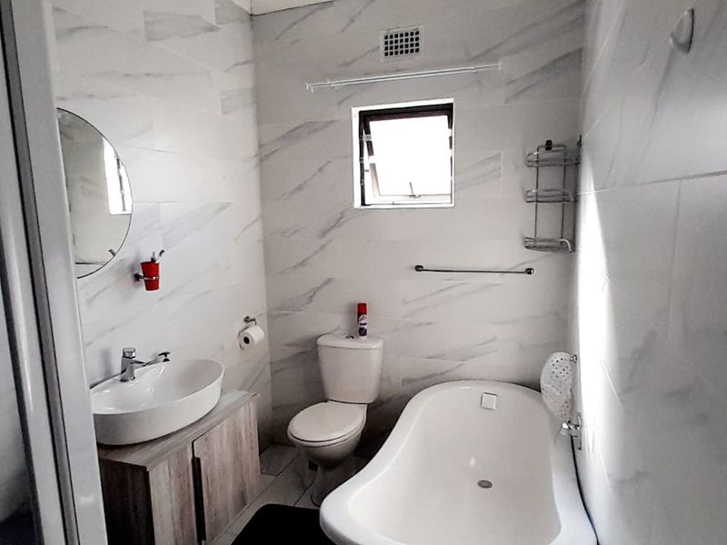 Modern bathroom featuring a freestanding bathtub, vessel sink with vanity cabinet, toilet, and a separate shower enclosure with marble-look wall tiles.