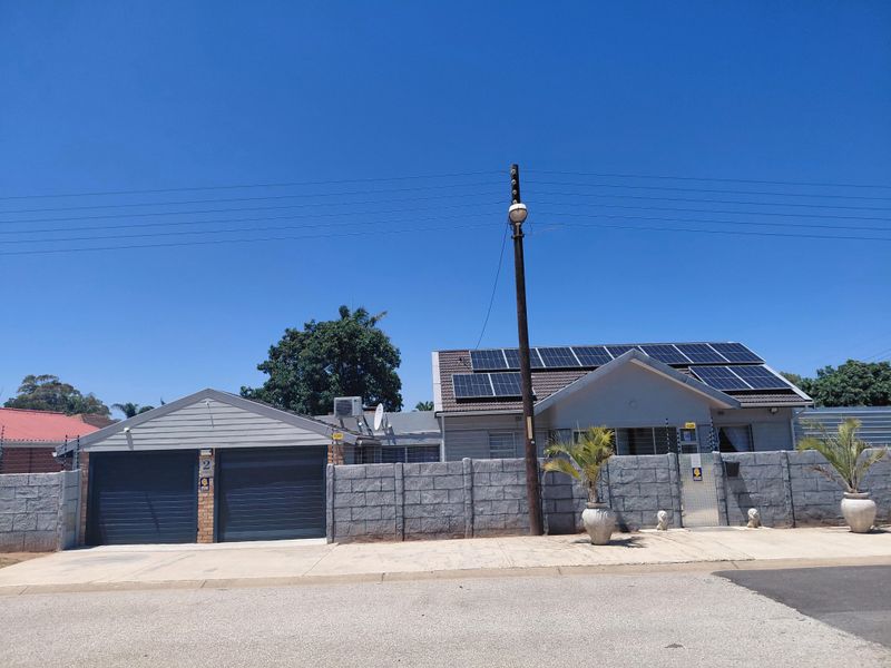 Front elevation of a residential property featuring a double garage, concrete block boundary wall, and roof-mounted solar panels under a clear blue sky.