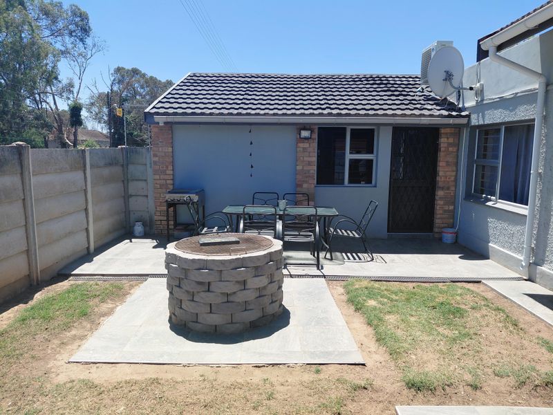 Outdoor patio area featuring a built-in stone fire pit, concrete paving, and a secure entrance, set within a private backyard with boundary walling.