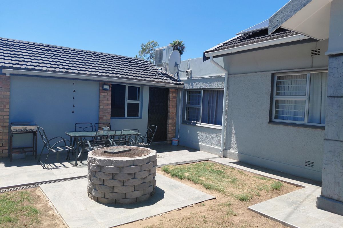 Rear exterior view featuring a paved patio area with a built-in brick fire pit, tiled roof, and aluminium window frames.