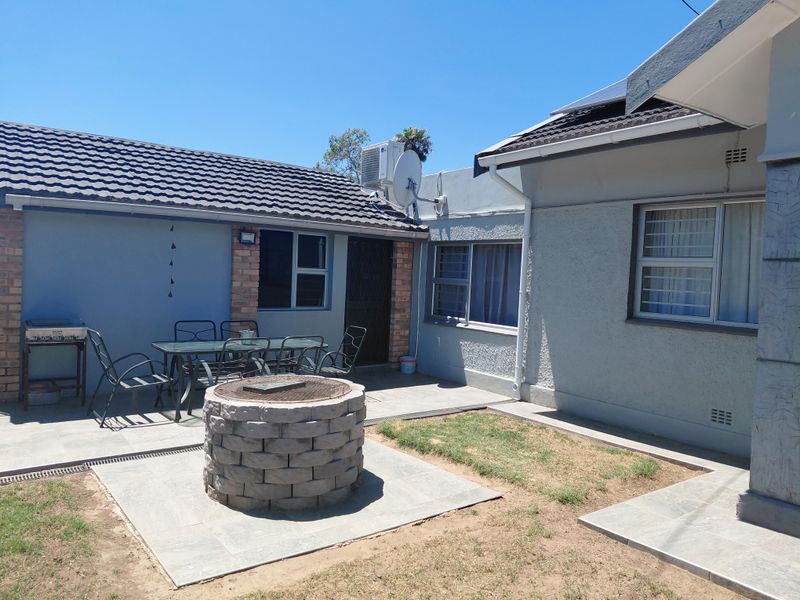 Rear exterior view featuring a paved patio area with a built-in brick fire pit, tiled roof, and aluminium window frames.