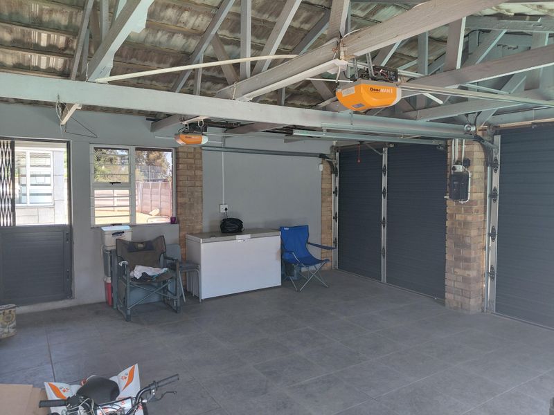 Spacious double garage featuring tiled flooring, exposed roof trusses, and secure roller doors, providing ample space for vehicle storage and utility use.
