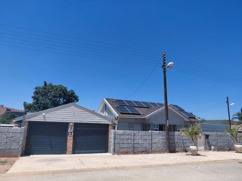 Front exterior view of a residential house featuring a double garage, concrete block boundary wall, and roof-mounted solar panels.