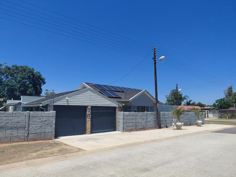 Front exterior view of a residential property featuring a double garage, tiled roof with solar panels, and a secure precast concrete boundary wall.