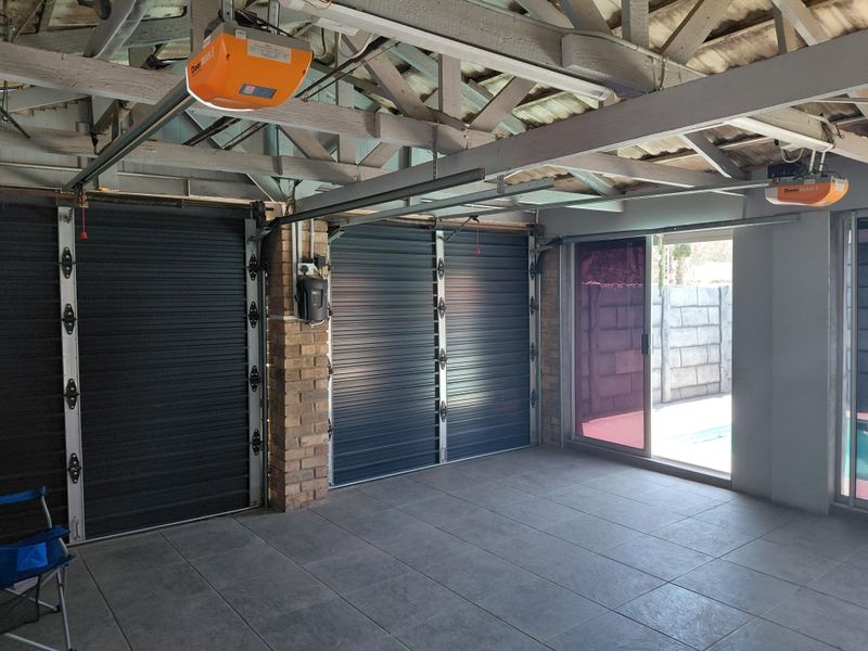 Spacious double garage featuring automated doors, exposed timber roof trusses, tiled flooring, and direct access to the outdoor pool area via a sliding door.