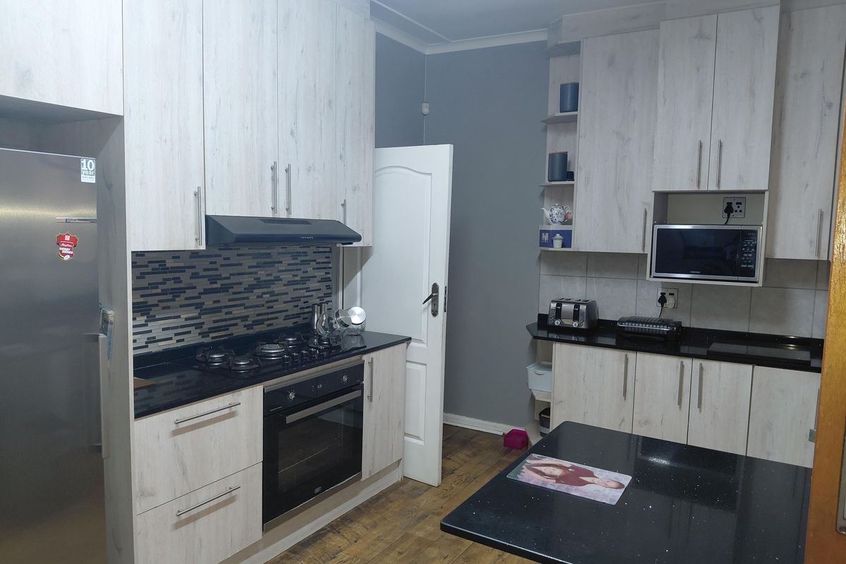 Modern kitchen featuring light wood-grain cabinetry, black granite countertops, a gas hob, built-in oven, and a mosaic tile backsplash.