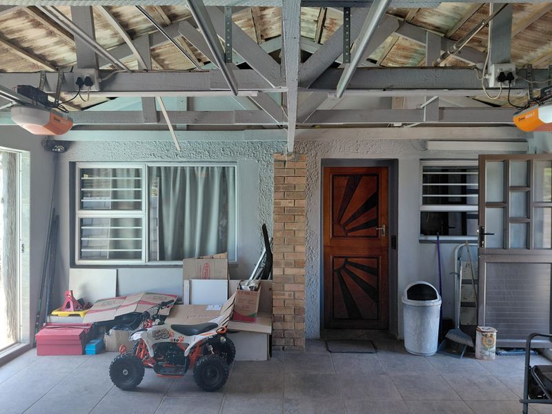 A functional garage space featuring exposed timber roof trusses, tiled flooring, and dual automated garage door motors.