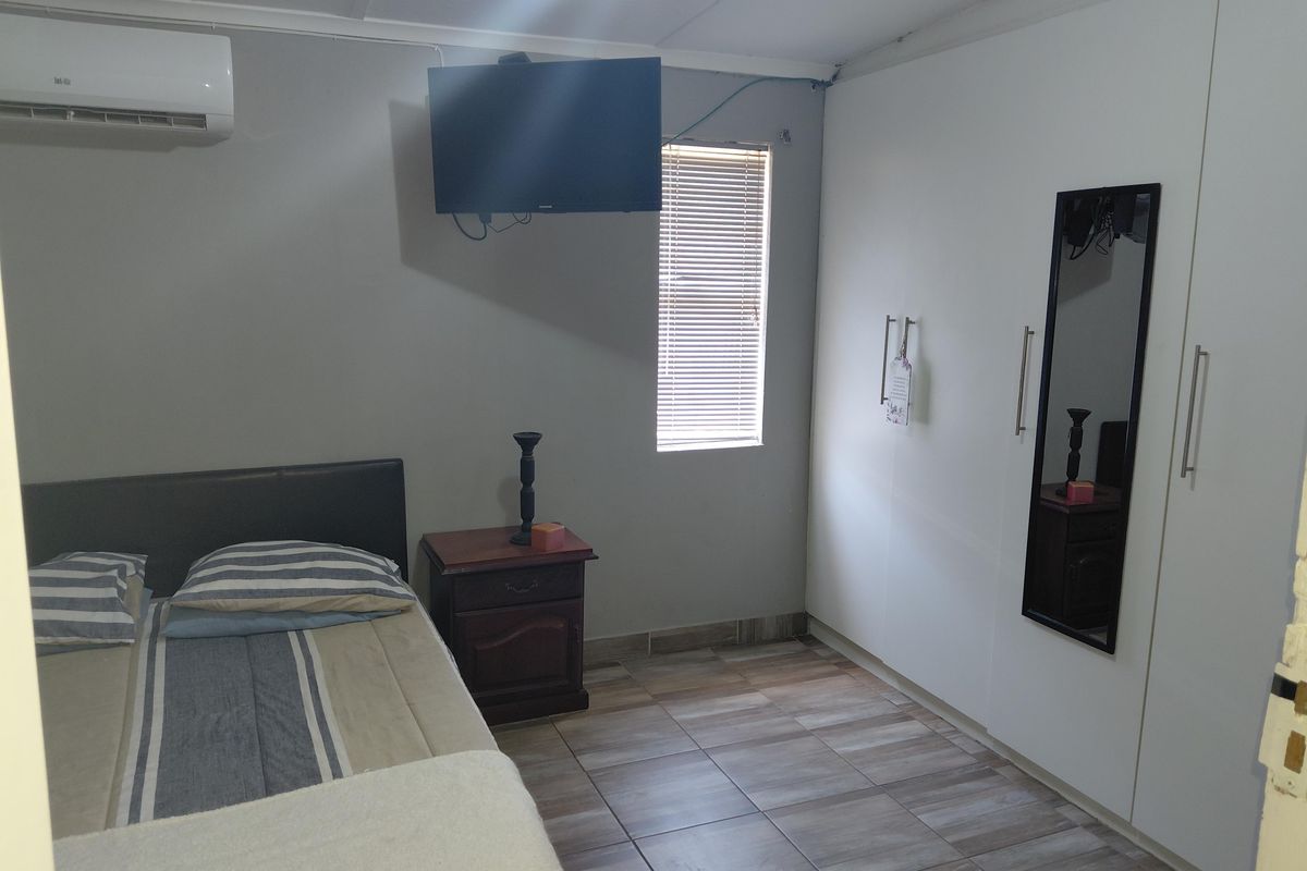 A functional bedroom featuring tiled flooring, a large built-in wardrobe, and a wall-mounted air conditioning unit.