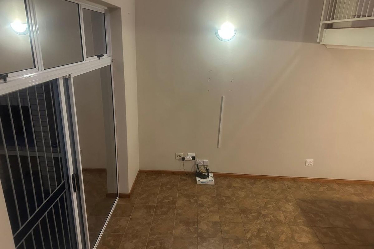 An empty living area featuring tiled flooring, a sliding glass door, and a staircase, requiring minor cosmetic updates to the walls.